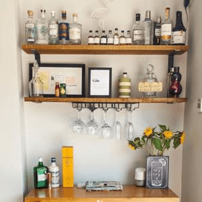 Wooden shelves with assorted liquor bottles, hanging wine glasses, framed art, and sunflower decor in home bar setup