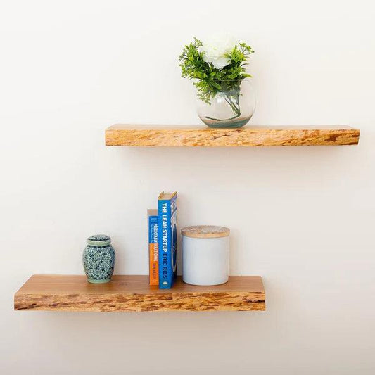 Minimalist wooden wall shelves with a glass vase of white flowers and greenery on top shelf, blue book, jar, and decorative ceramic pot on bottom shelf