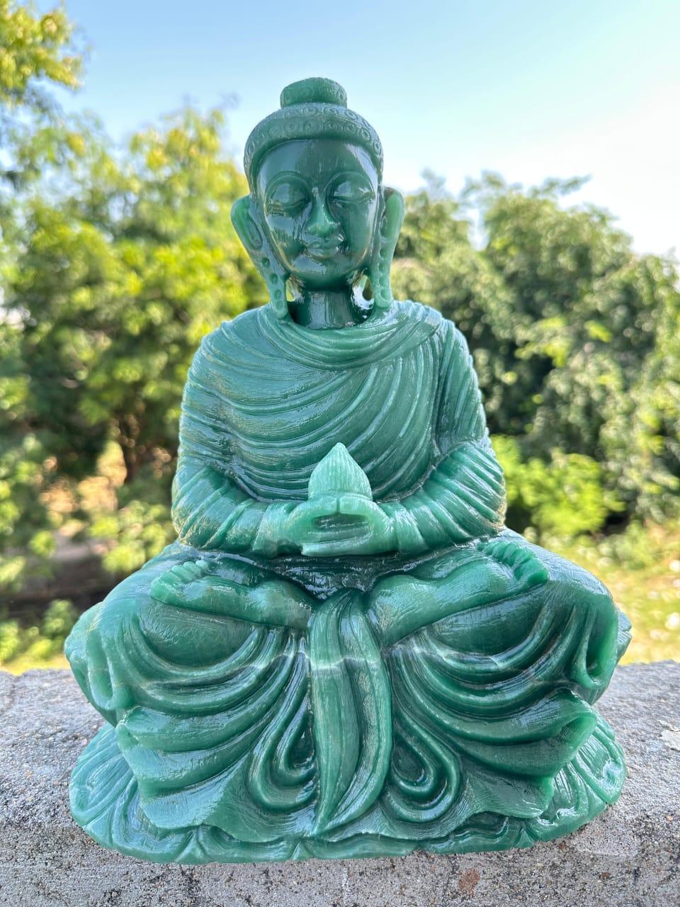 Green jade Buddha statue in meditation pose placed outdoors with trees and clear sky background