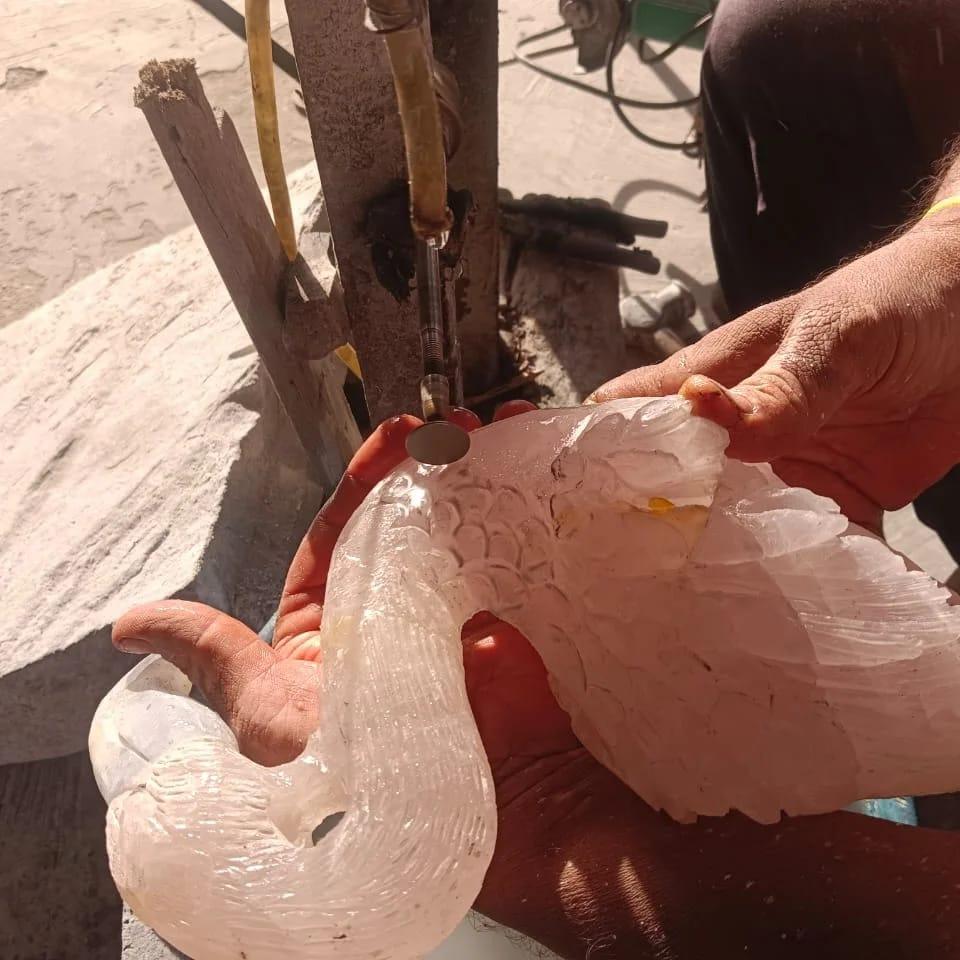 Artisan carving a detailed white marble swan sculpture by hand in a workshop
