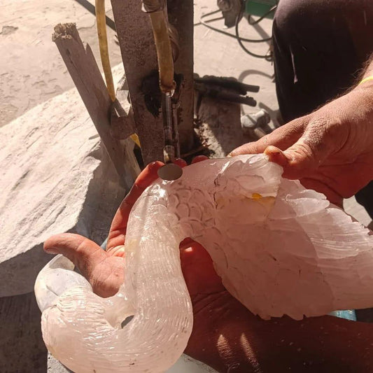 Artisan carving a detailed white marble swan sculpture by hand in a workshop