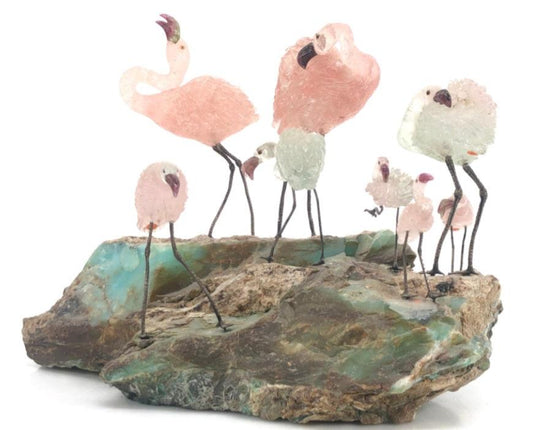 Sculpture of pink flamingos with wire legs standing on a green and brown mineral rock base